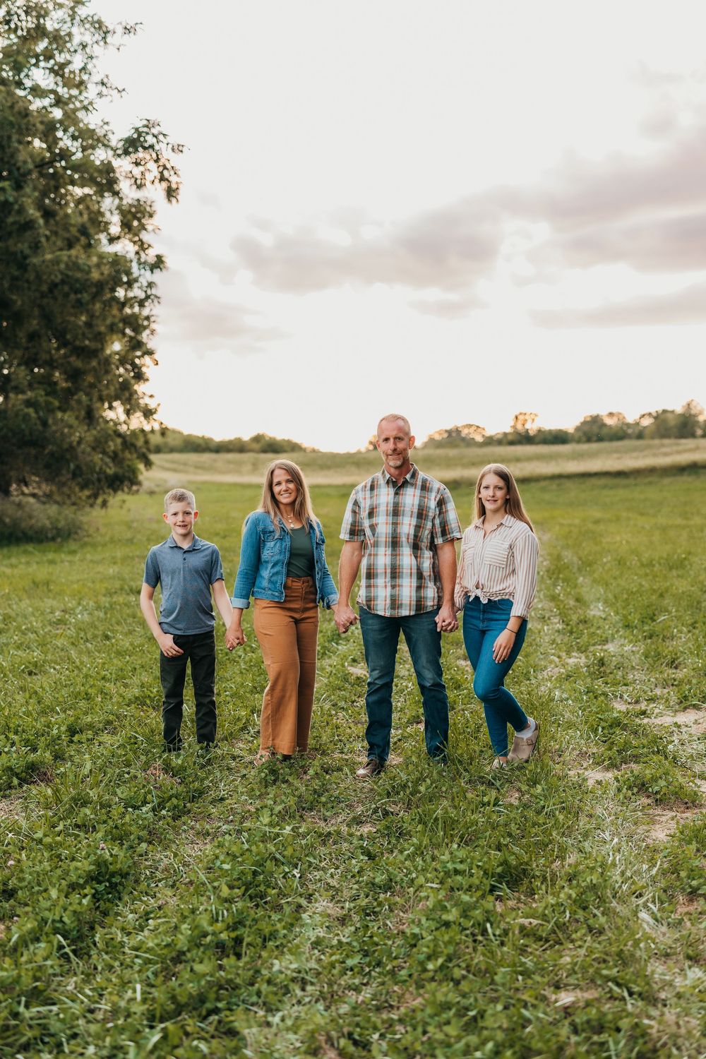 Group walking together through a serene meadow during sunset wearing coordinated blue and brown outfits.