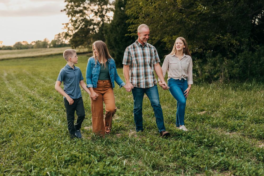 Family walking together through a lush green field at sunset during a casual outdoor photoshoot.