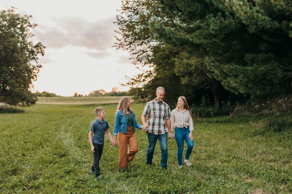 A group walking together in a grassy field at sunset with trees in the background.
