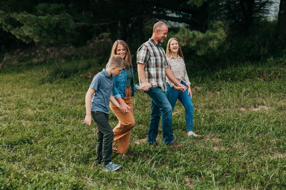 Family walking together through a grassy field at sunset, holding hands and laughing.
