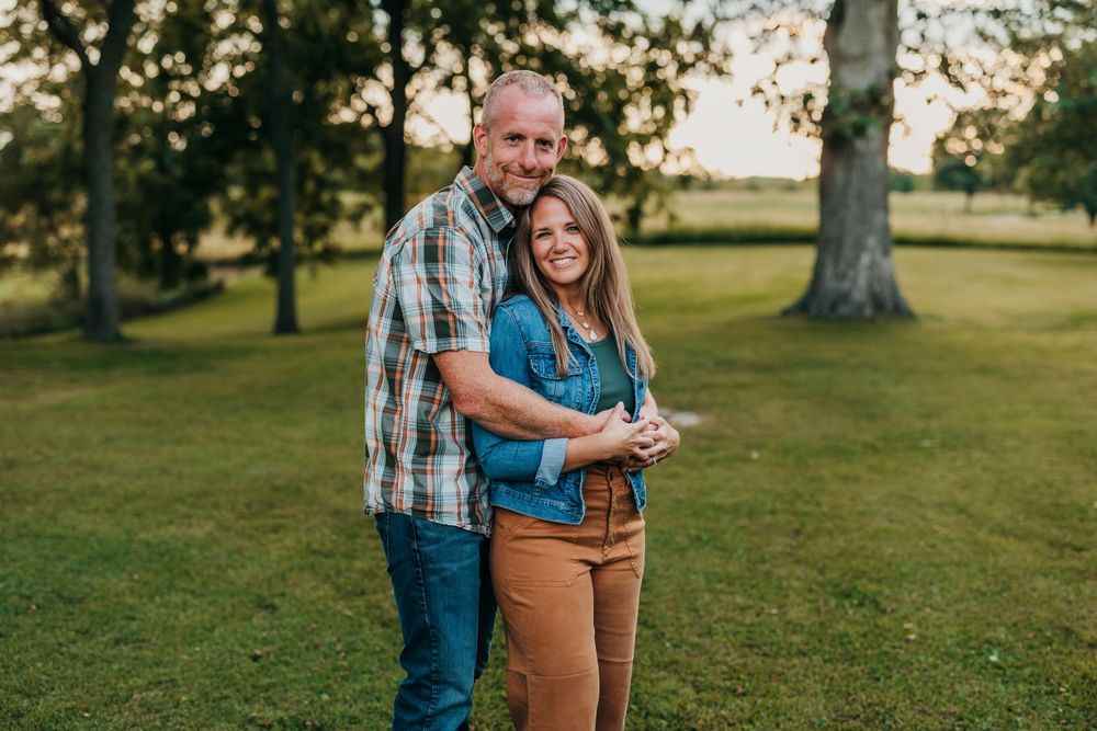 A family group poses warmly together in an orchard setting with trees in the background.