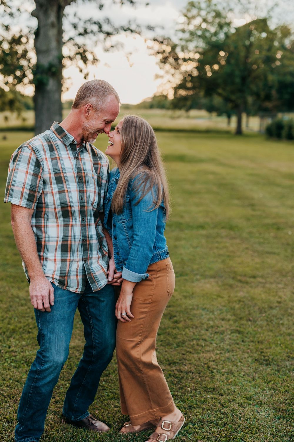 Couple in casual clothing sharing tender moments in a sunny park setting.