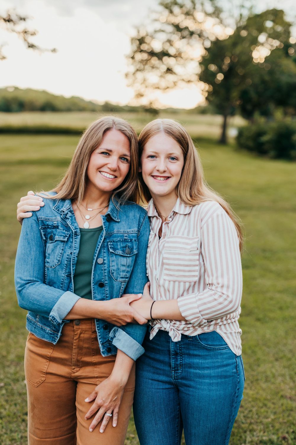 Two people share joyful moment together on sunny field wearing denim and earth tones.