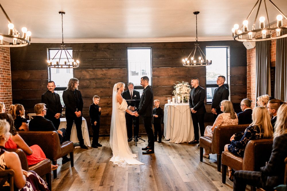 Bride and groom exchanging vows under wooden arch with greenery
