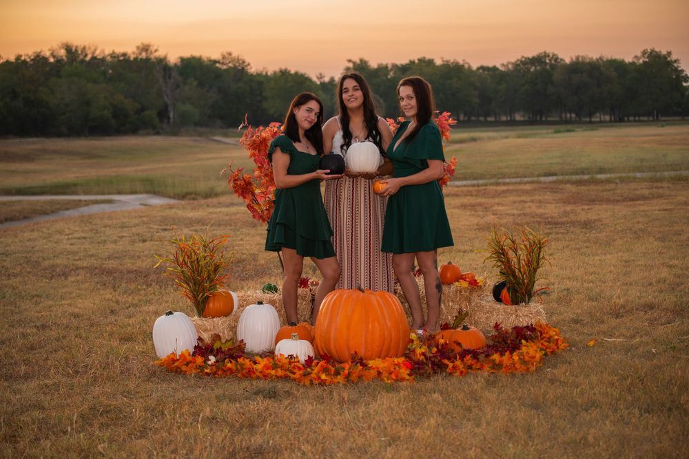 Fall scene with green dresses and autumn decor featuring pumpkins, dried flowers and white vases at golden sunset.