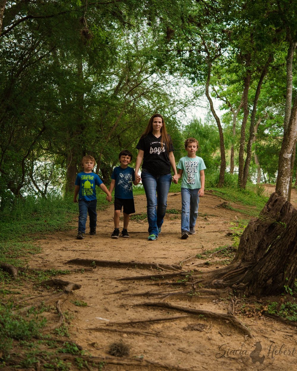A group of people walking along a winding dirt trail through a lush green forest on a sunny day.