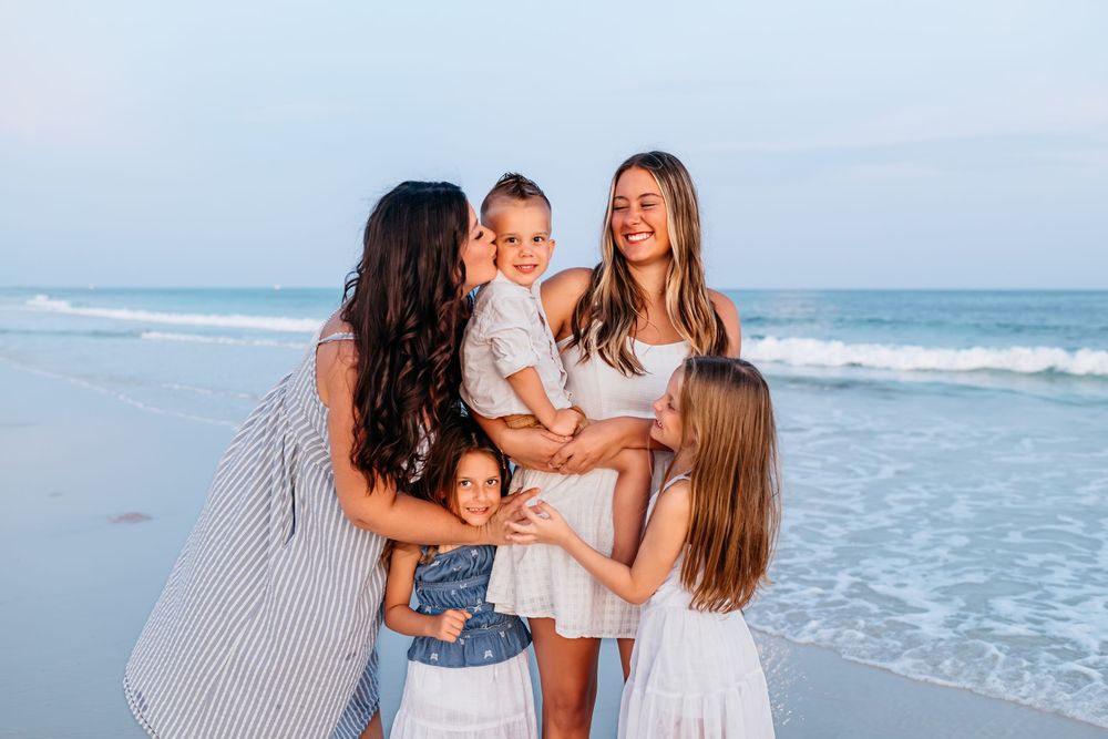 A group enjoying a casual moment together on the beach at sunset with ocean waves in the background.