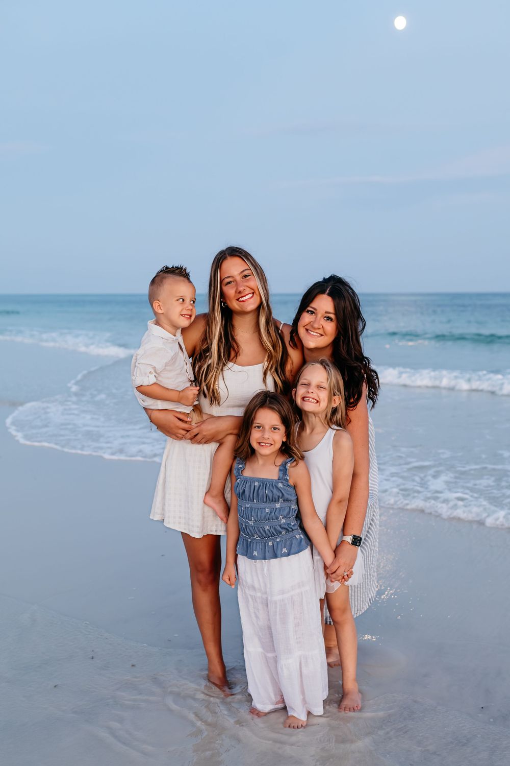 People posing together on a sandy beach at sunset with ocean waves in the background.