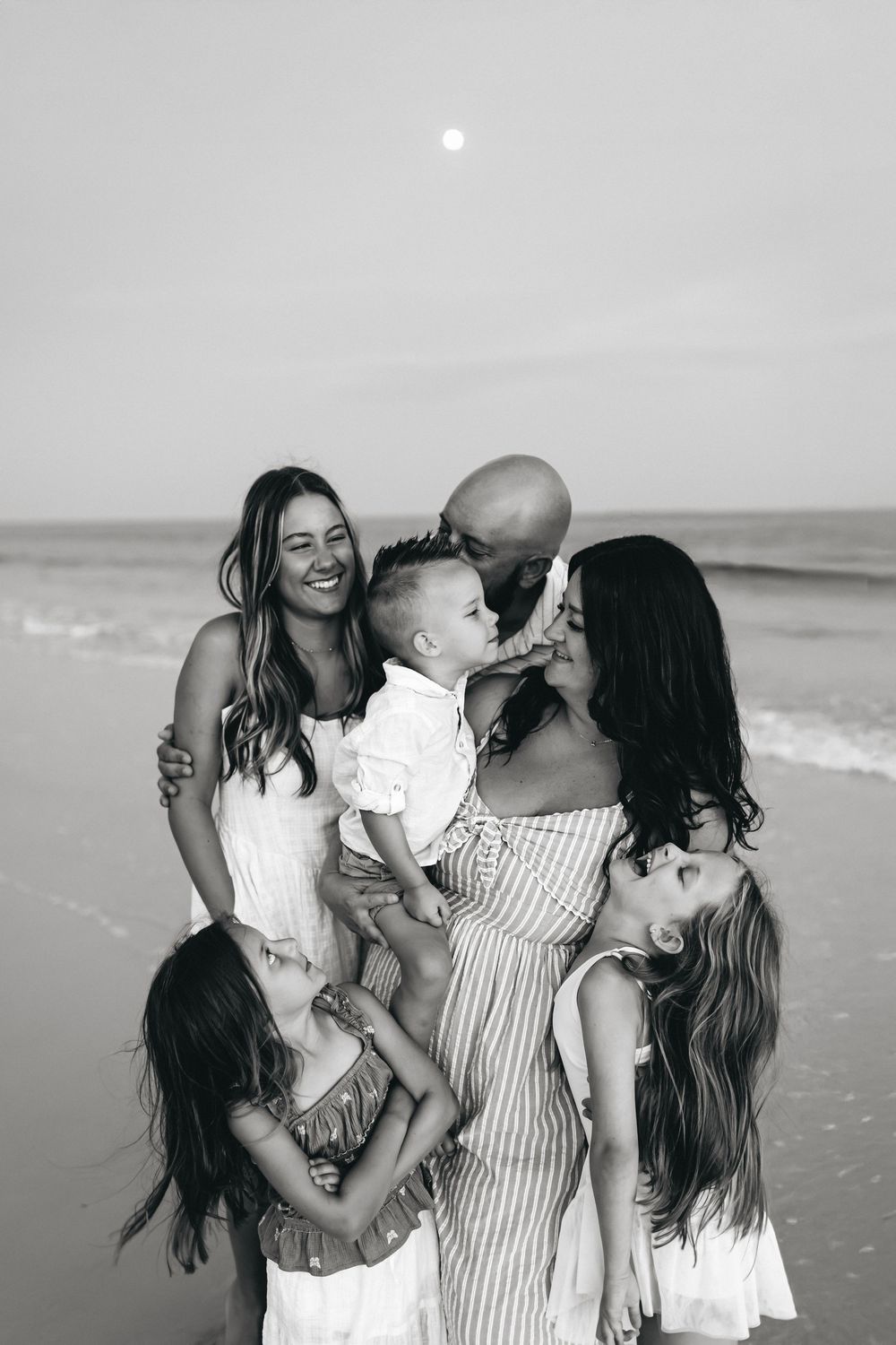 A family shares tender moments on the beach in black and white as they embrace and play together.