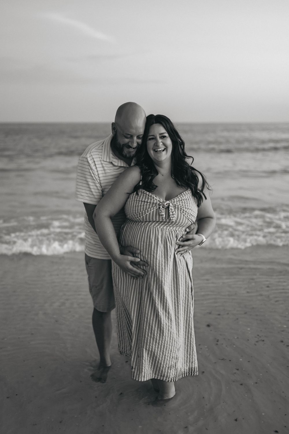 A couple embraces while walking along a beach shore in black and white photography.