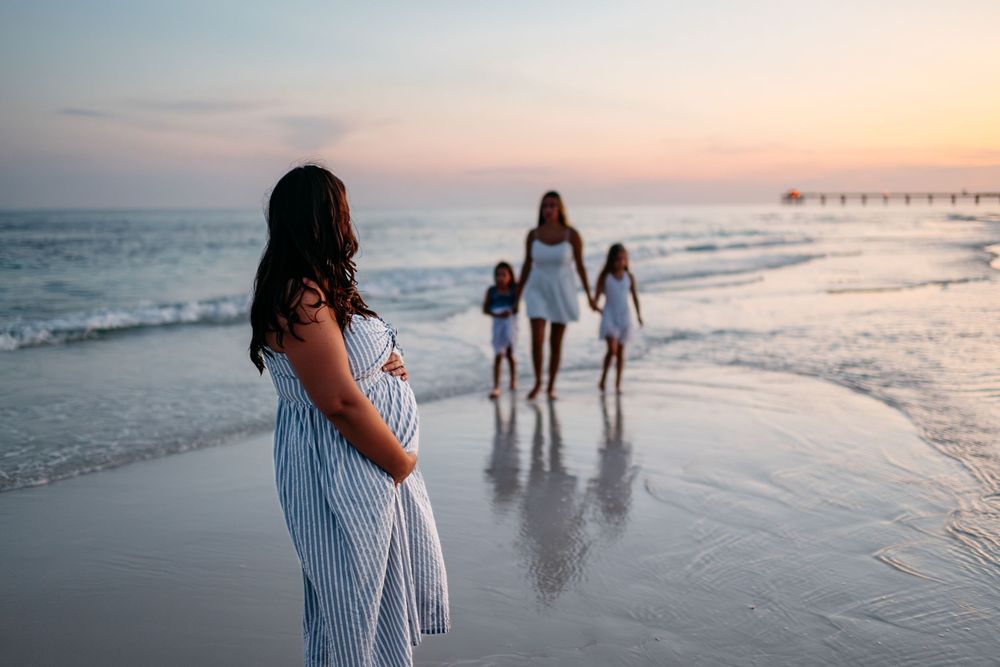 Silhouettes of people walking along beach shoreline at sunset with warm orange sky reflecting on wet sand.