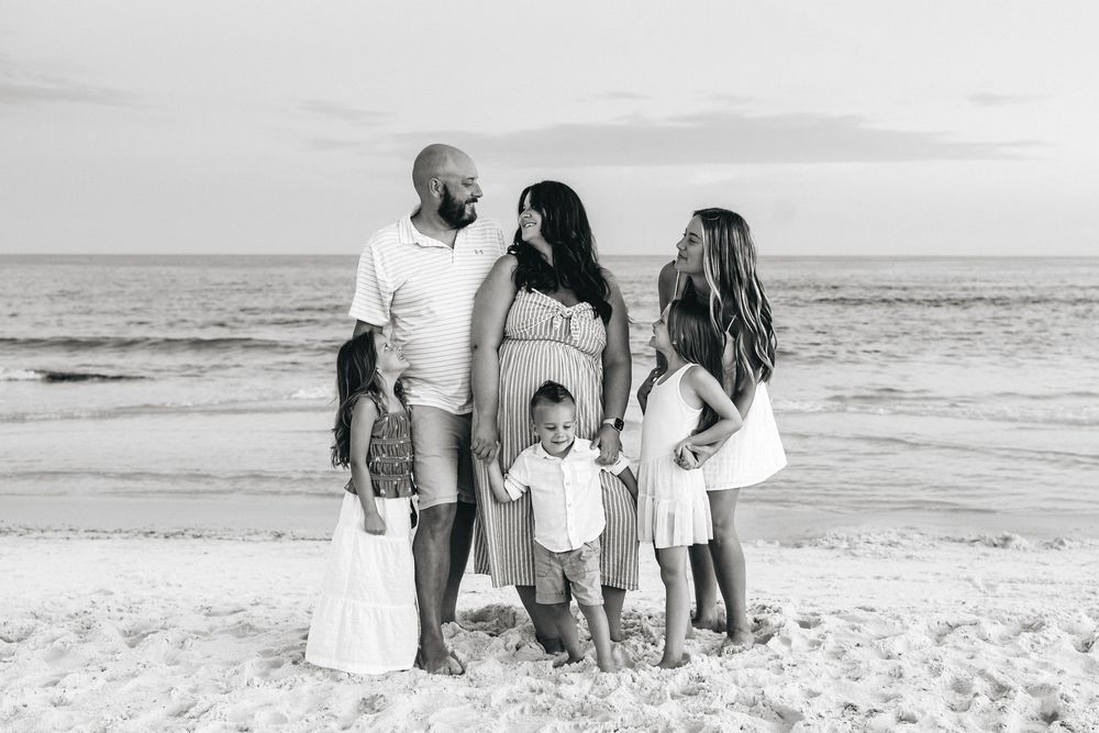 Group of people walking on a white sandy beach by the ocean shoreline in black and white photography.