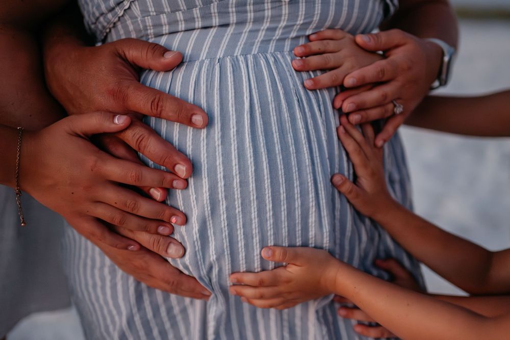 Multiple hands gently rest on a pregnant belly covered in striped fabric.