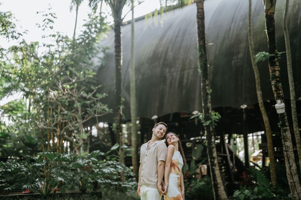 A couple walks hand in hand through a lush tropical garden path.
