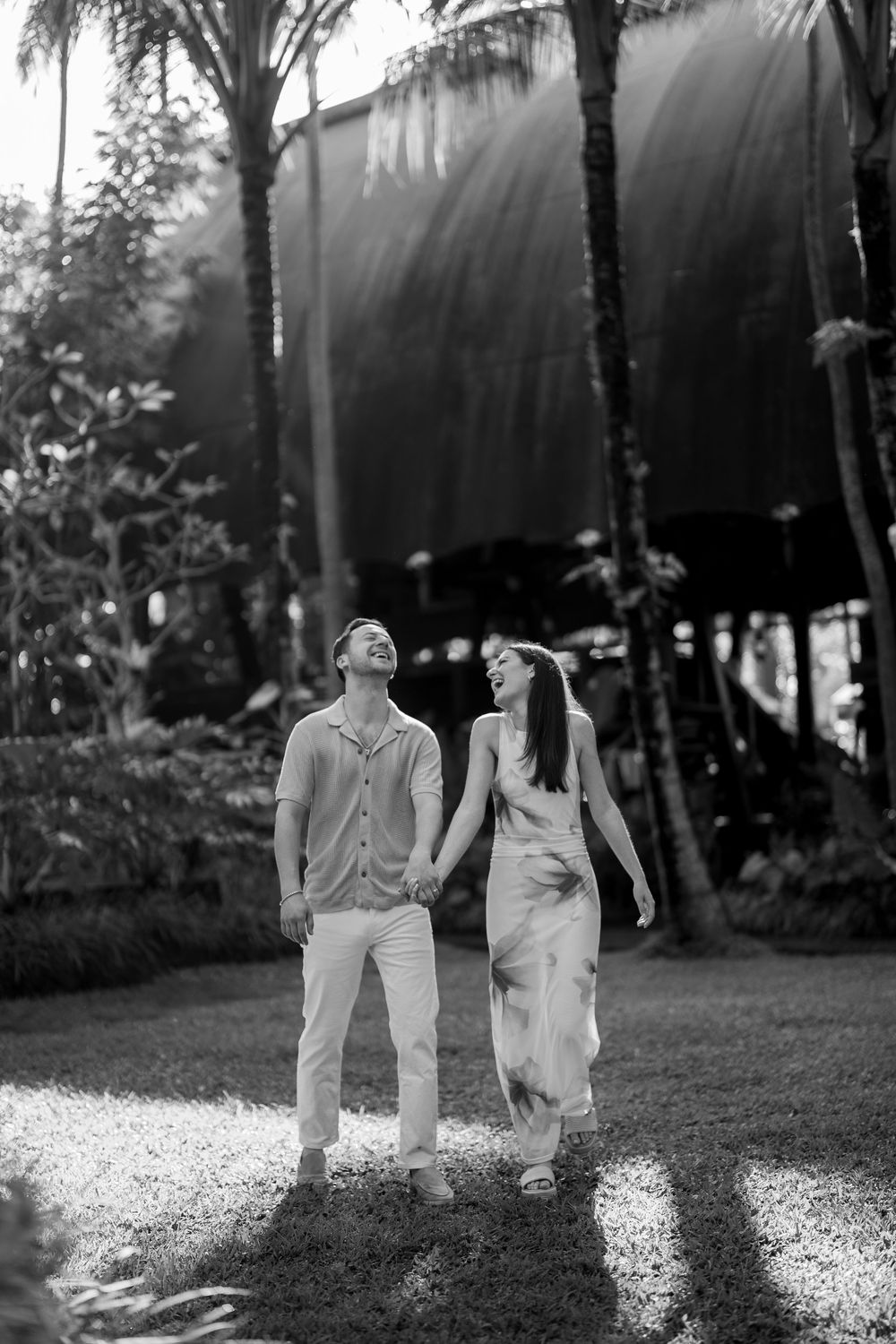 A couple walks through a sunlit garden path creating long shadows on the ground.