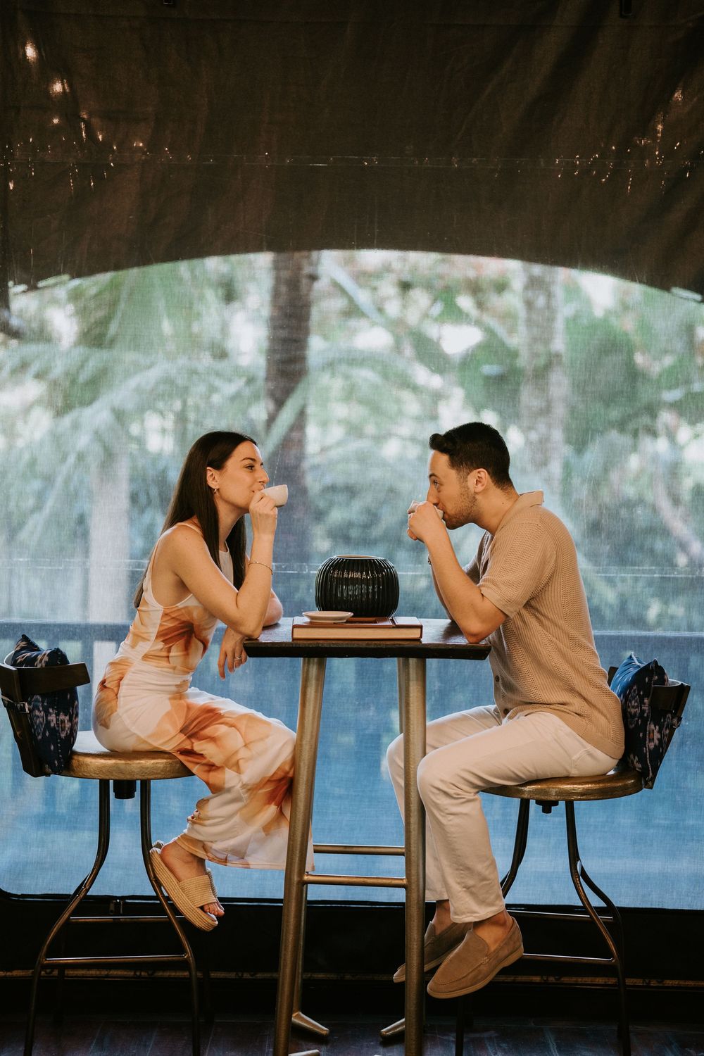 A couple shares a playful moment while sitting at a table in an outdoor setting.