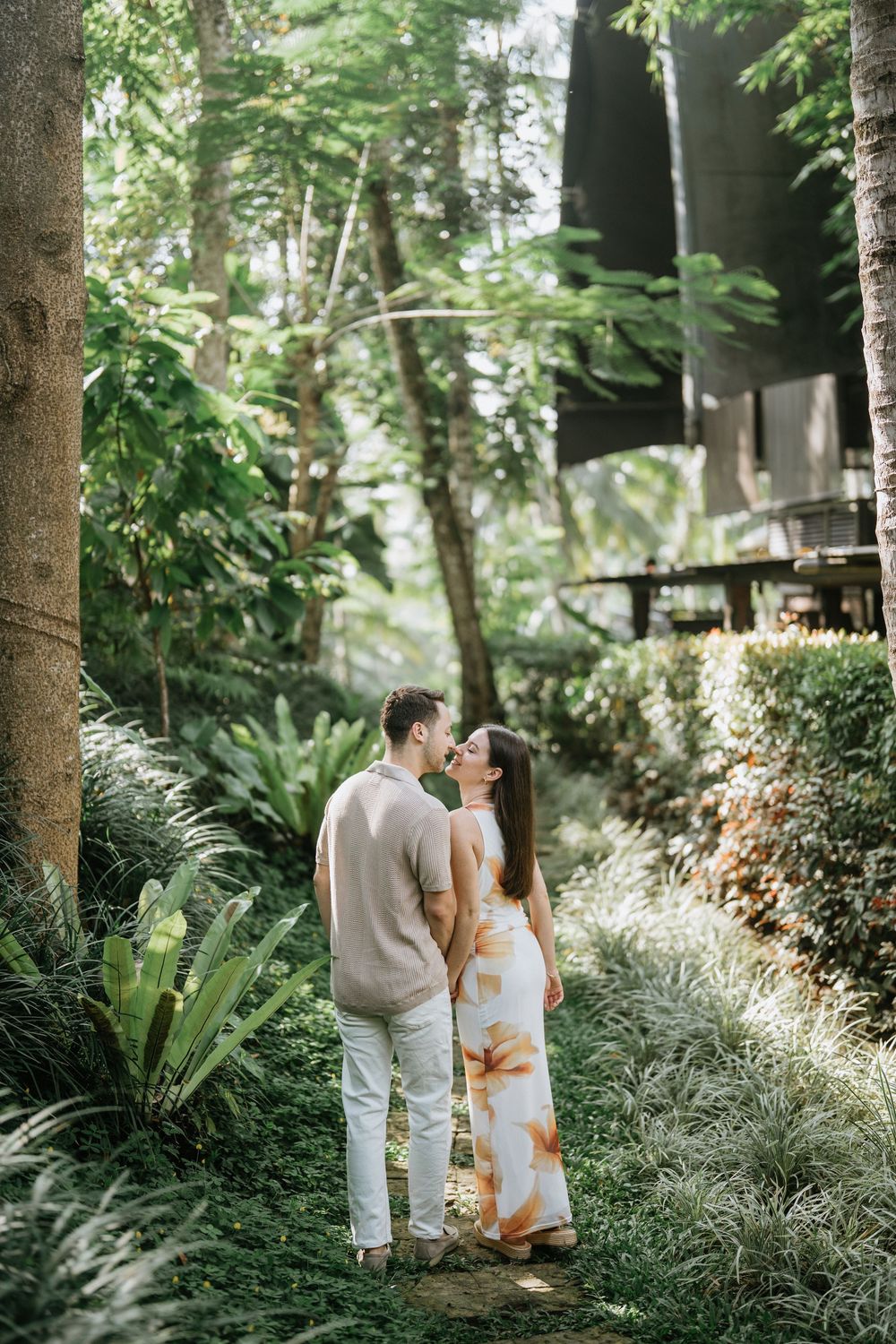 A couple walks through a tropical garden pathway surrounded by lush greenery.