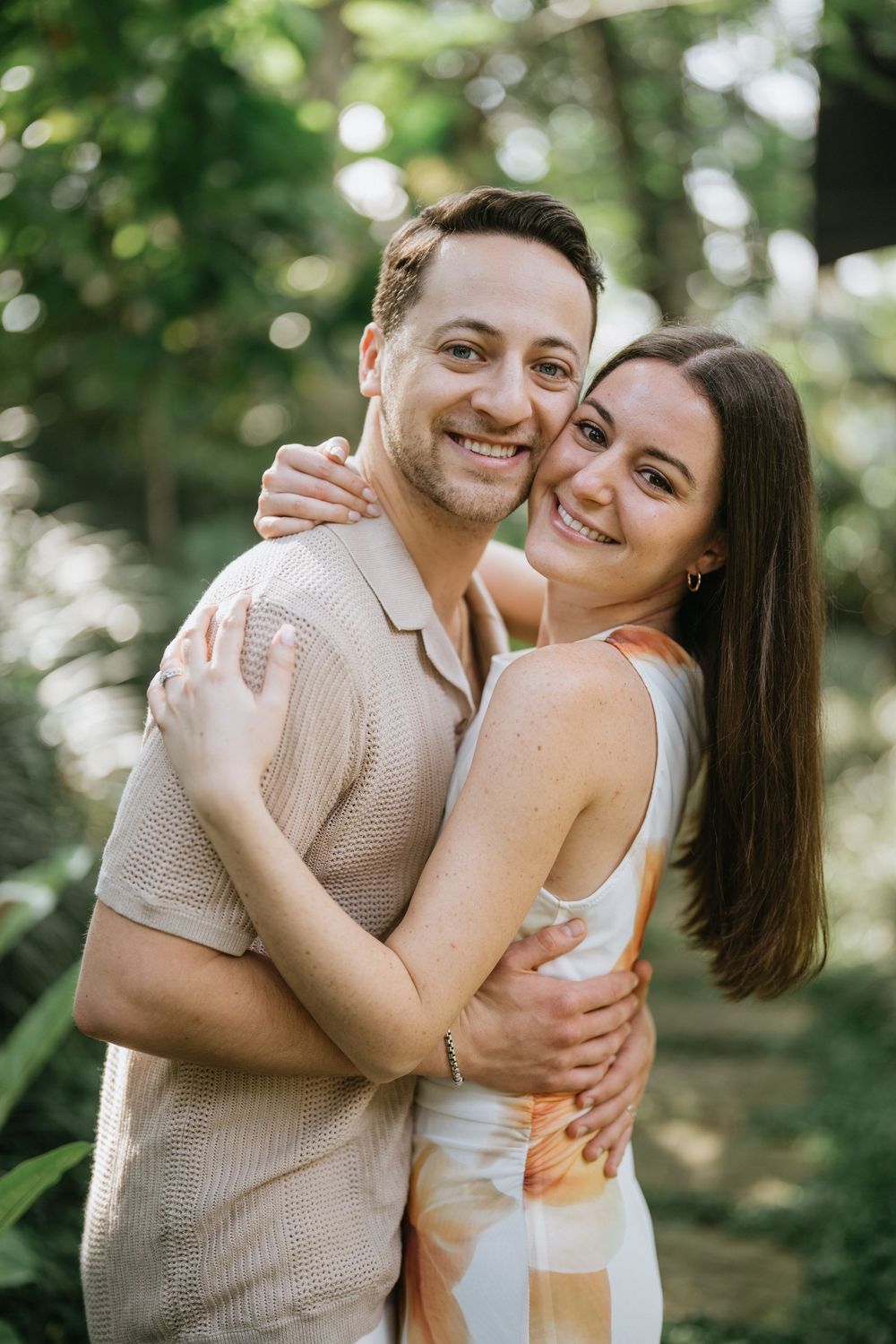 A couple embraces and laughs together in a sunny outdoor garden setting.