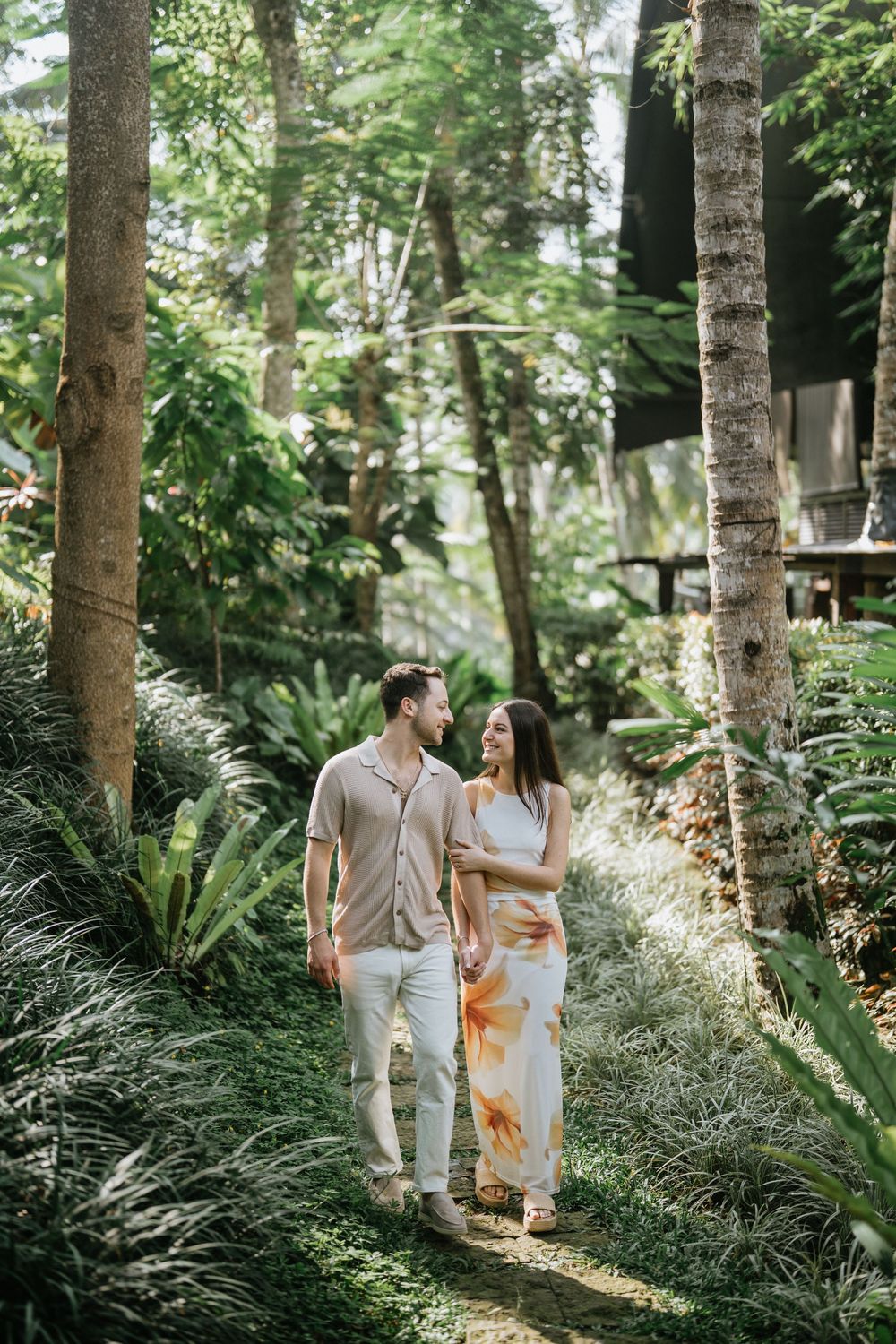 A couple walks together through a serene forest path lined with tall trees.