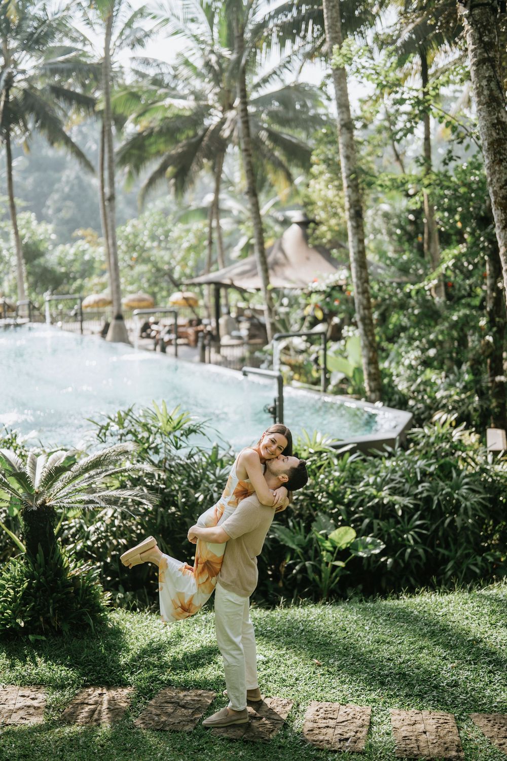 A couple shares a playful moment in a tropical garden with palm trees.