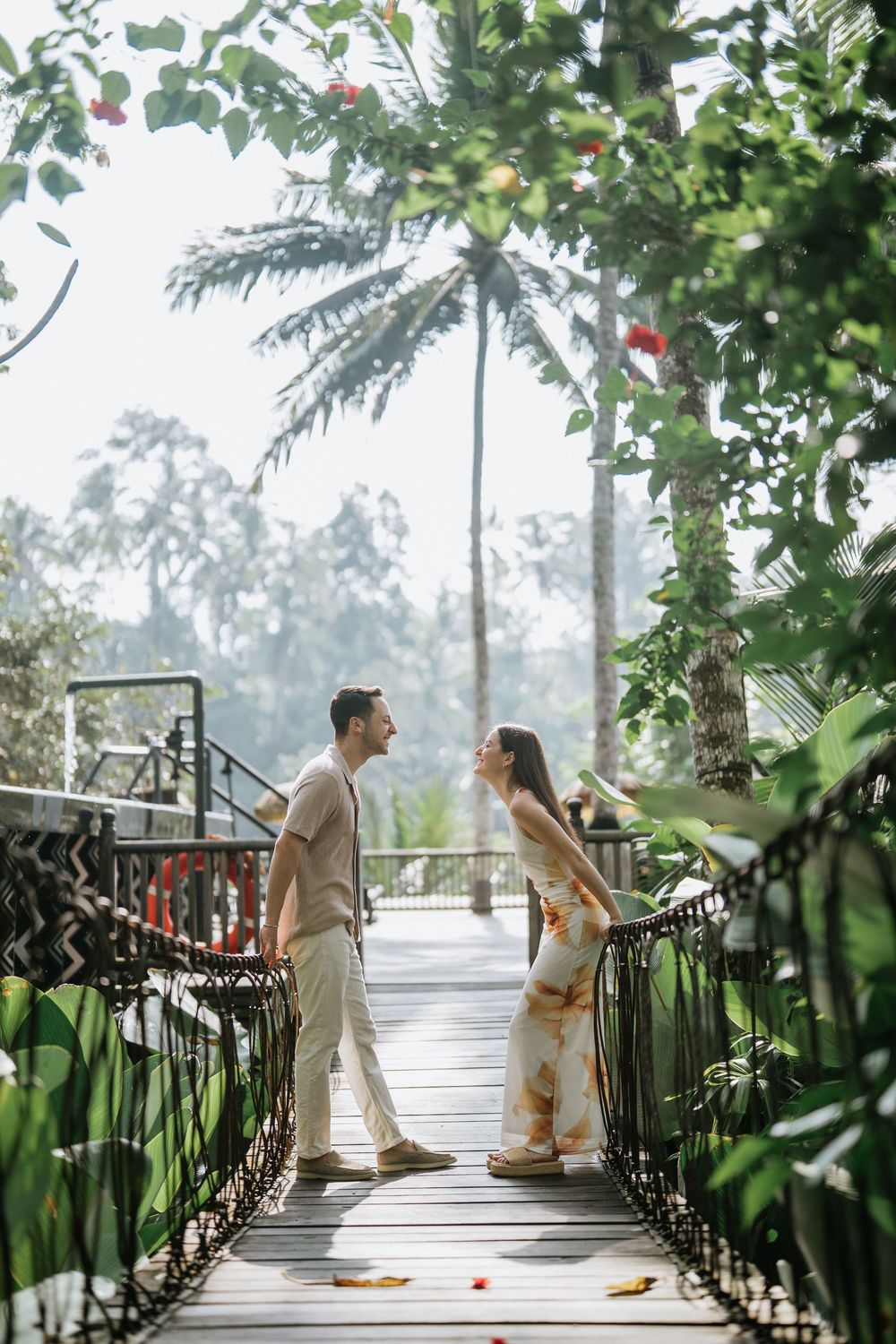 A couple poses on a bridge surrounded by lush tropical gardens and palm trees.