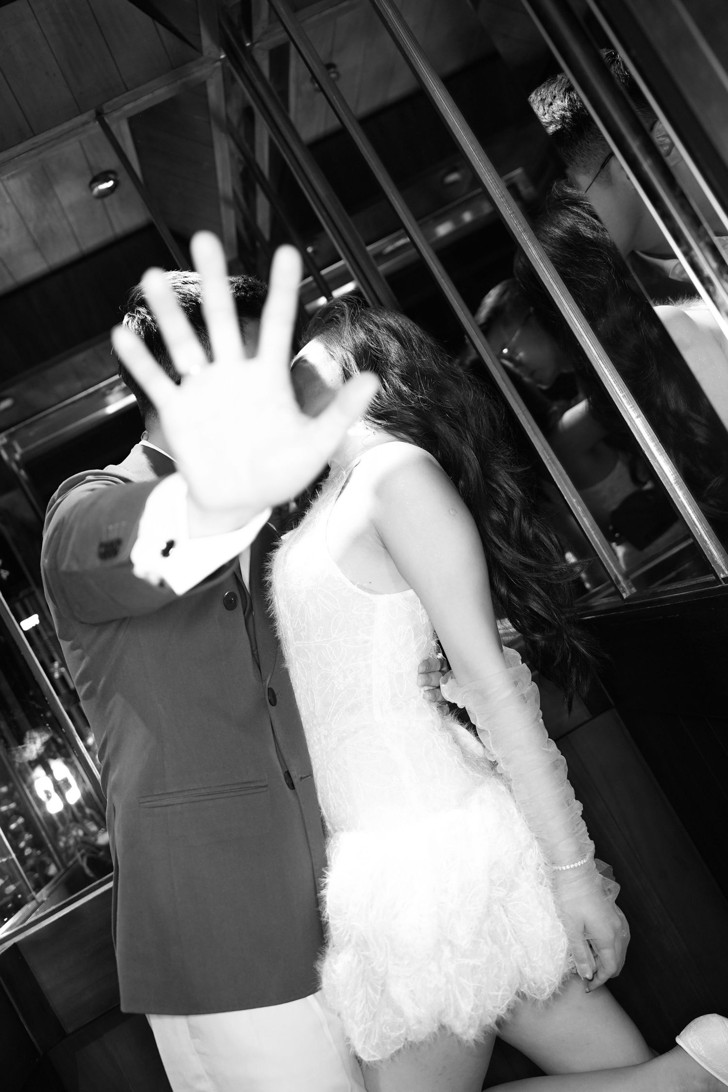 Black and white photo of a couple kissing, man playfully blocking camera with his hand.