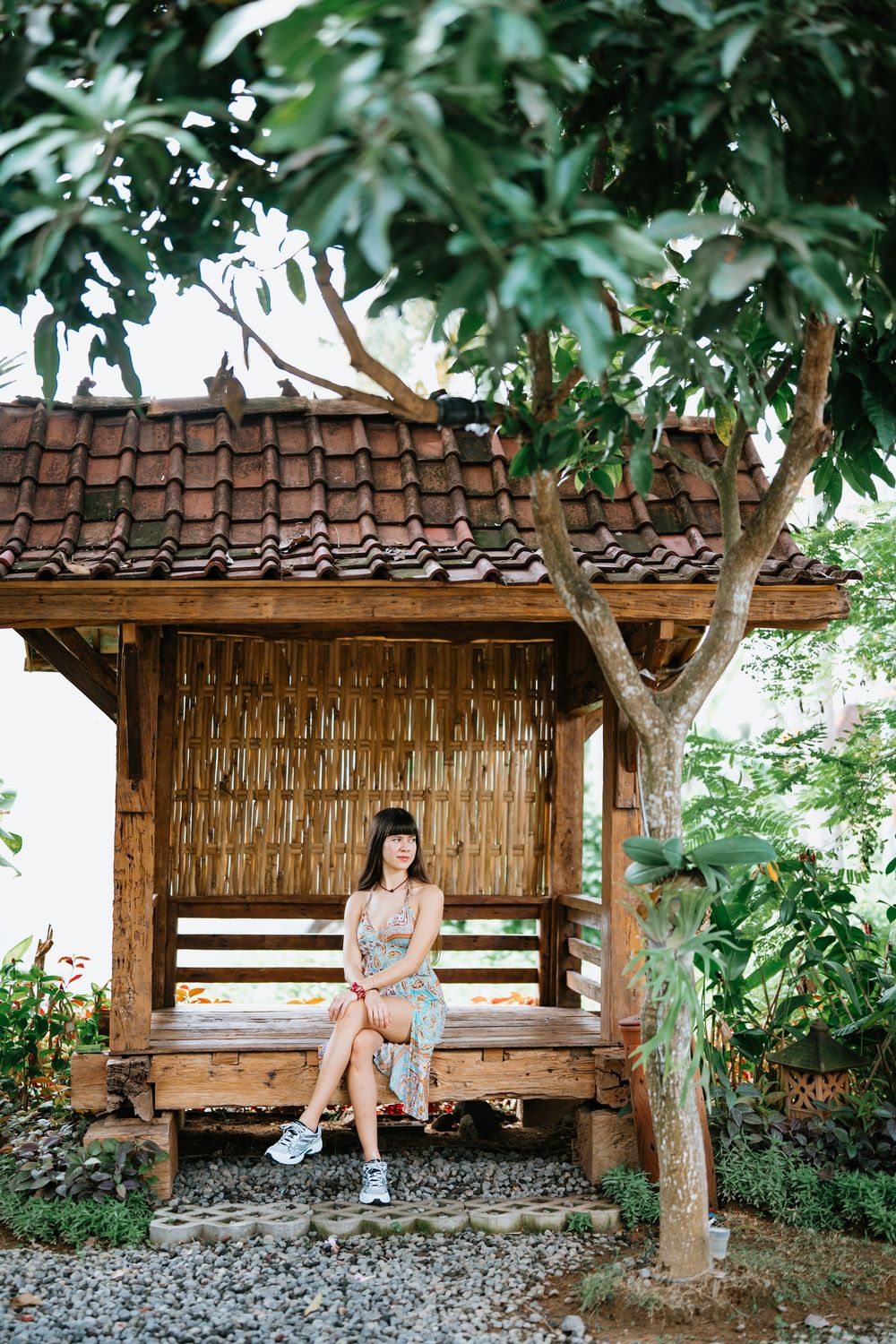 Traditional wooden gazebo surrounded by lush tropical garden and stone pathway.