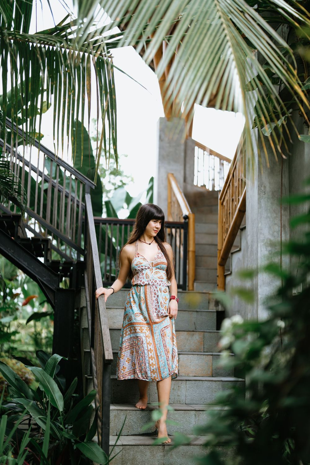 A floral summer dress is captured in a series of shots on wooden stairs surrounded by tropical palm fronds.