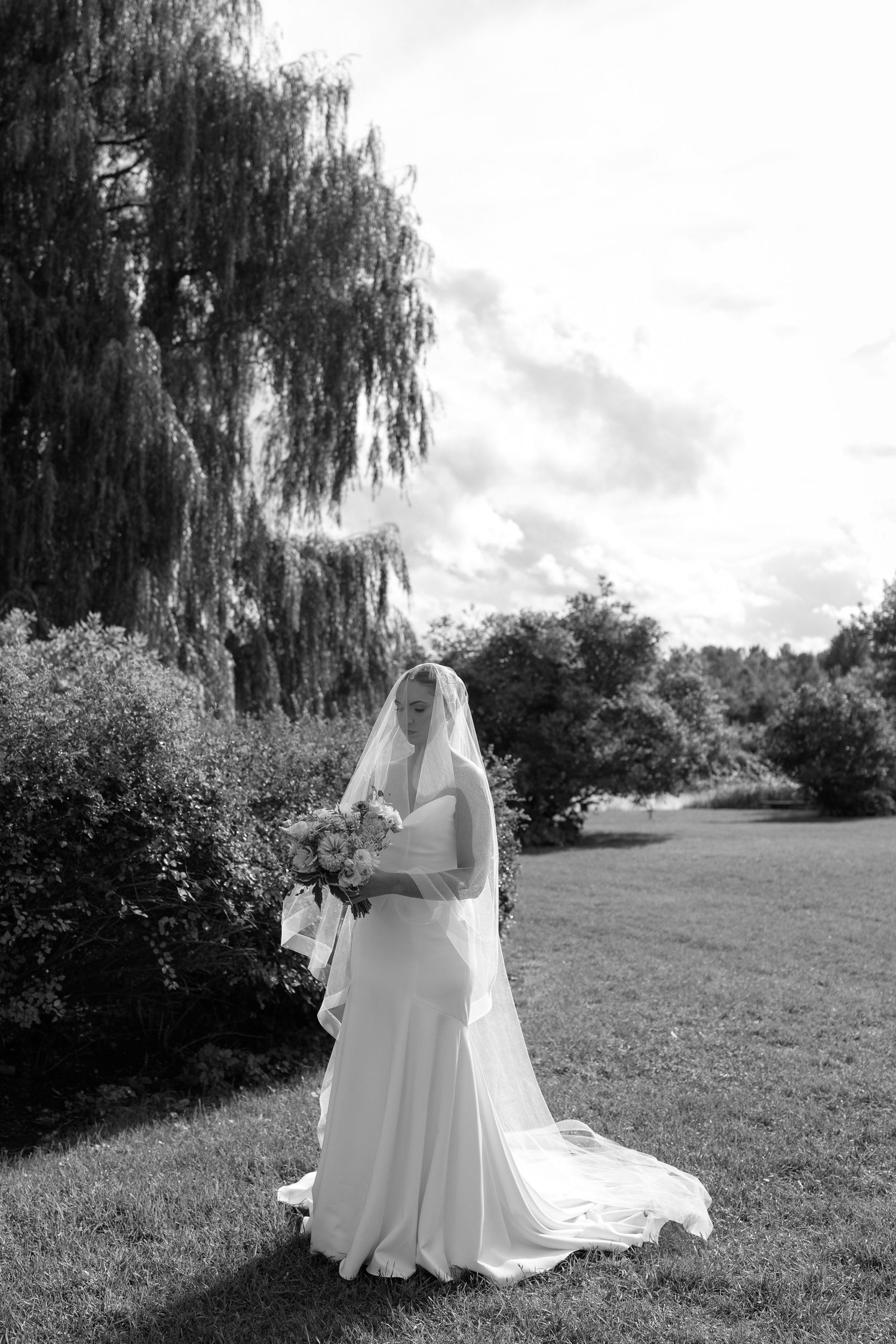 A black and white bridal portrait series showing a figure in a flowing white wedding gown standing in a grassy field.