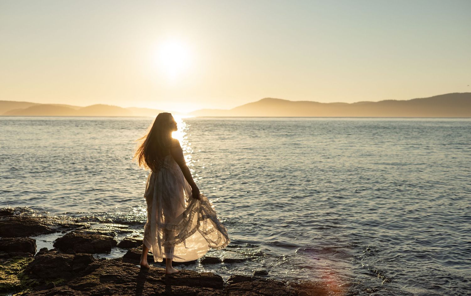 Woman dancing by the water at sunset at Washington Park in Anacortes, WA.
