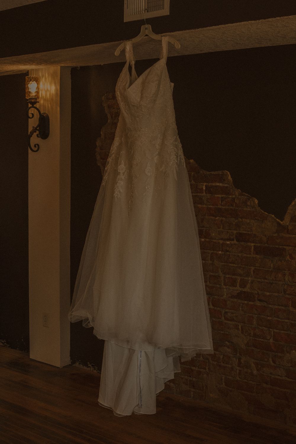 A white wedding dress hangs elegantly against an exposed brick wall.