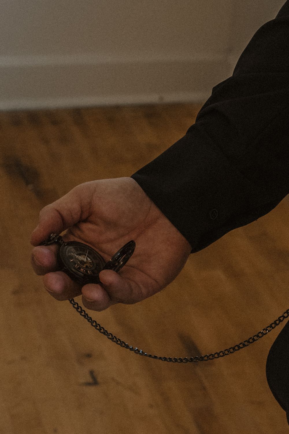Hands holding a vintage pocket watch with chain against a wooden floor background.