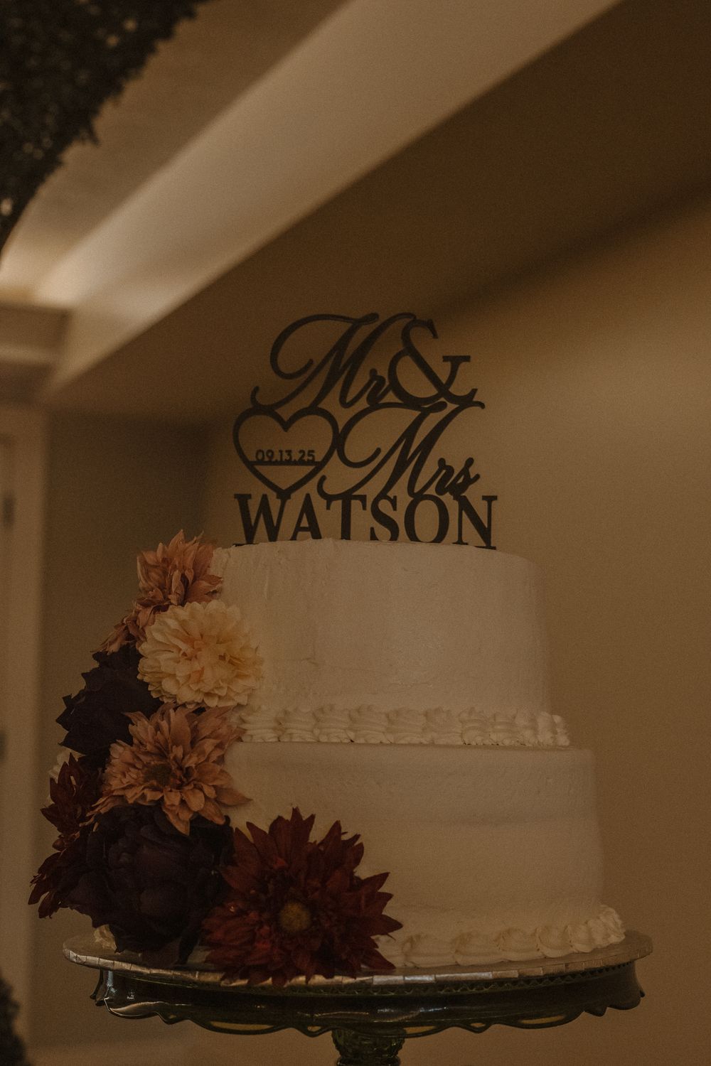 Wedding cake decorated with Mr and Mrs text topper and autumn-colored flowers.