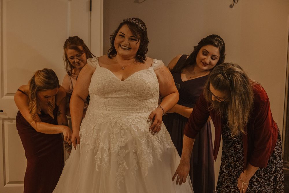 A wedding party gathers in a room wearing burgundy dresses and a white bridal gown.