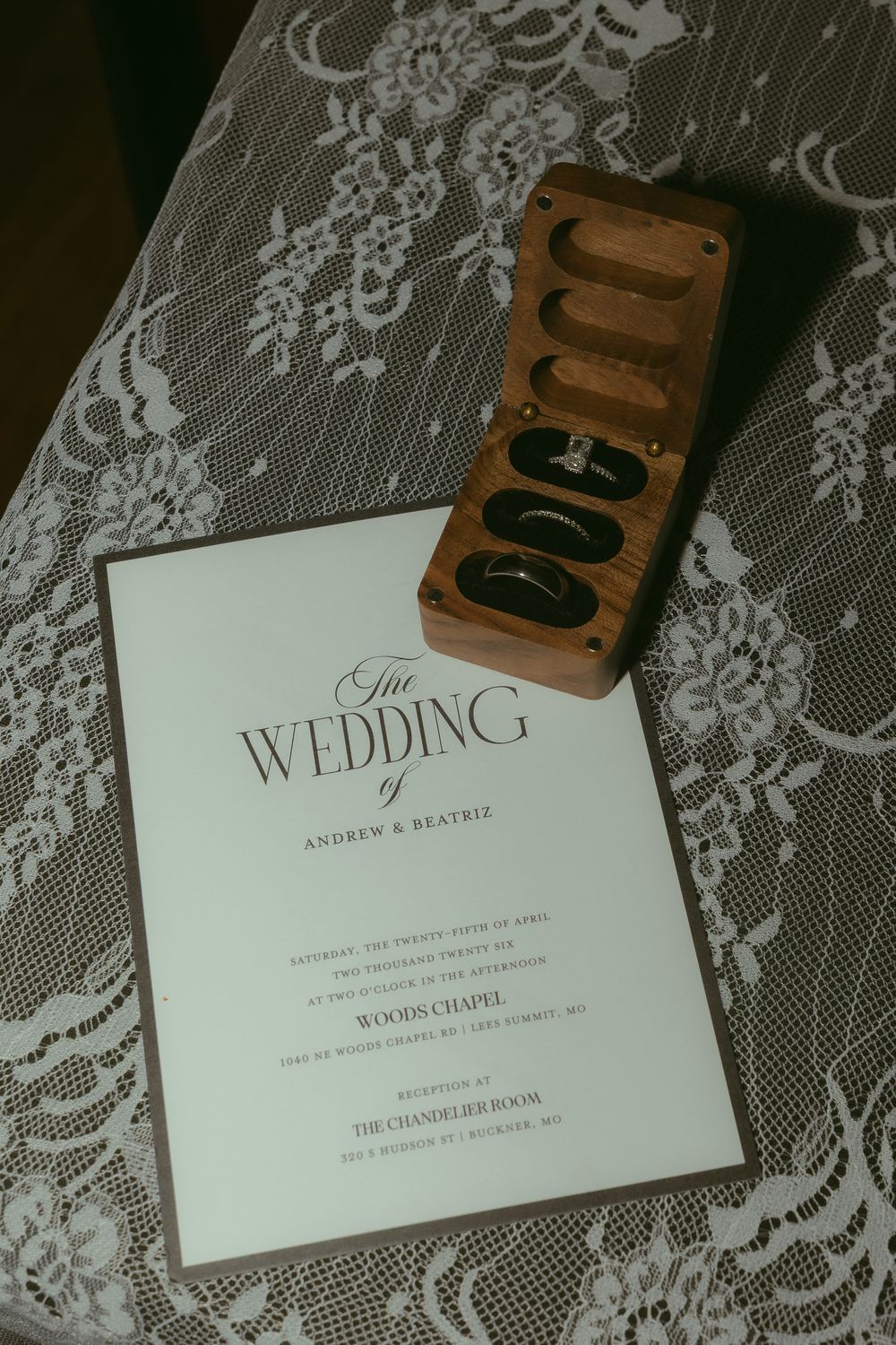Elegant wedding program for Andrew and Beatriz at Woods Chapel beside a wooden ring box with wedding bands on lace.
