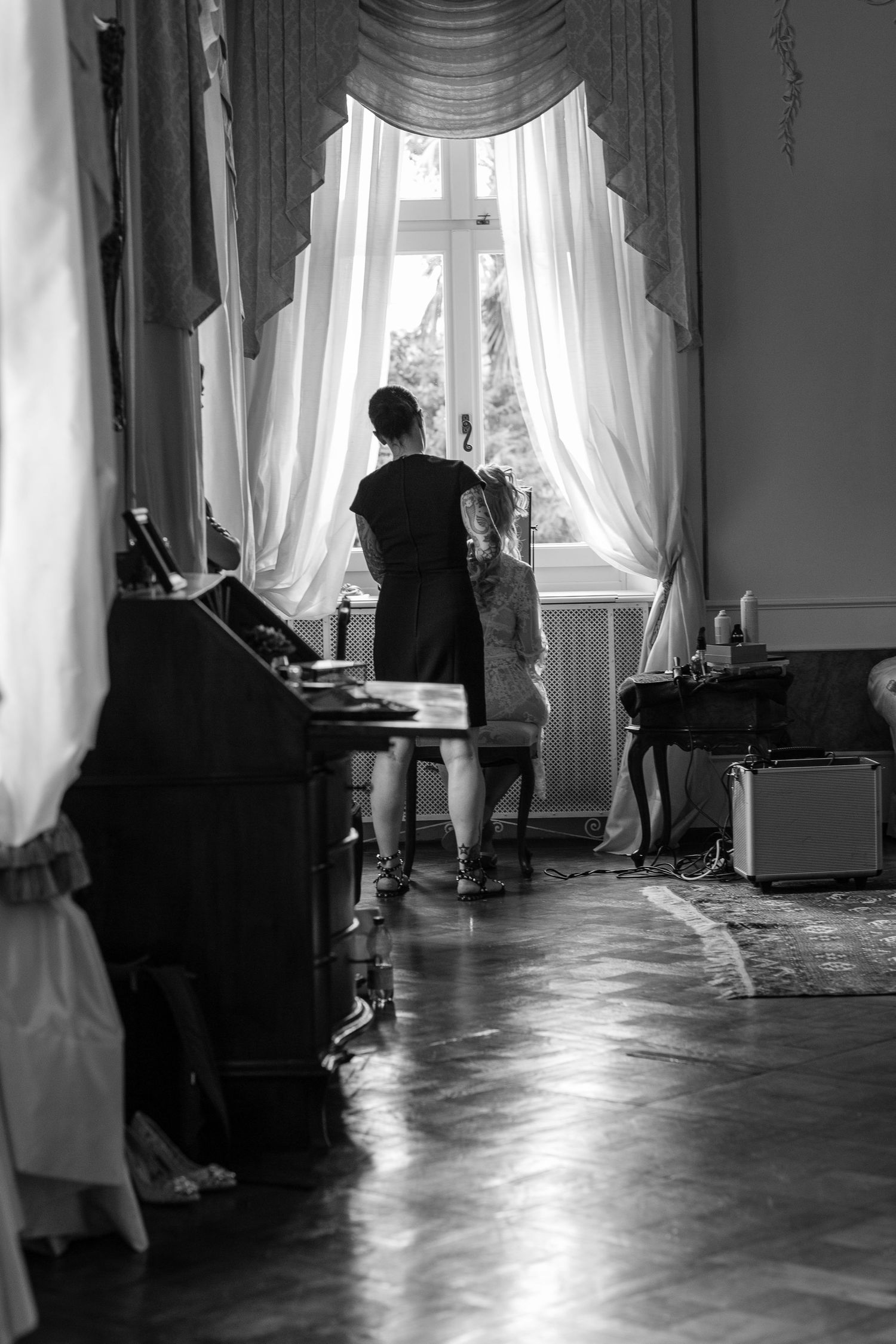 Sunlight streams through white curtained windows into an elegant room with wooden floors.