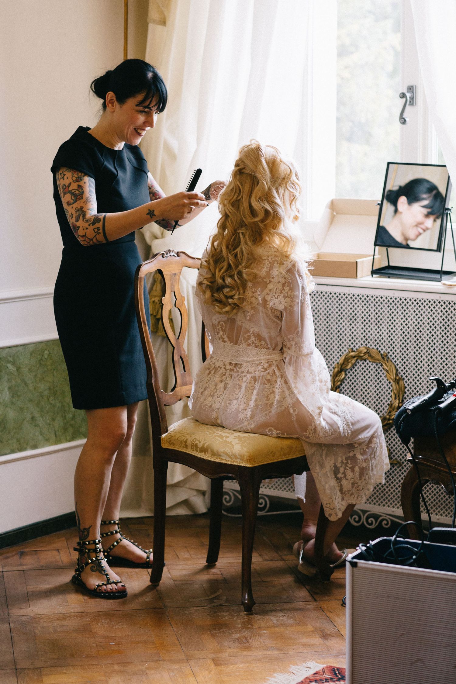 Stylist preparing a client for an event in an elegant dressing room with antique furniture.