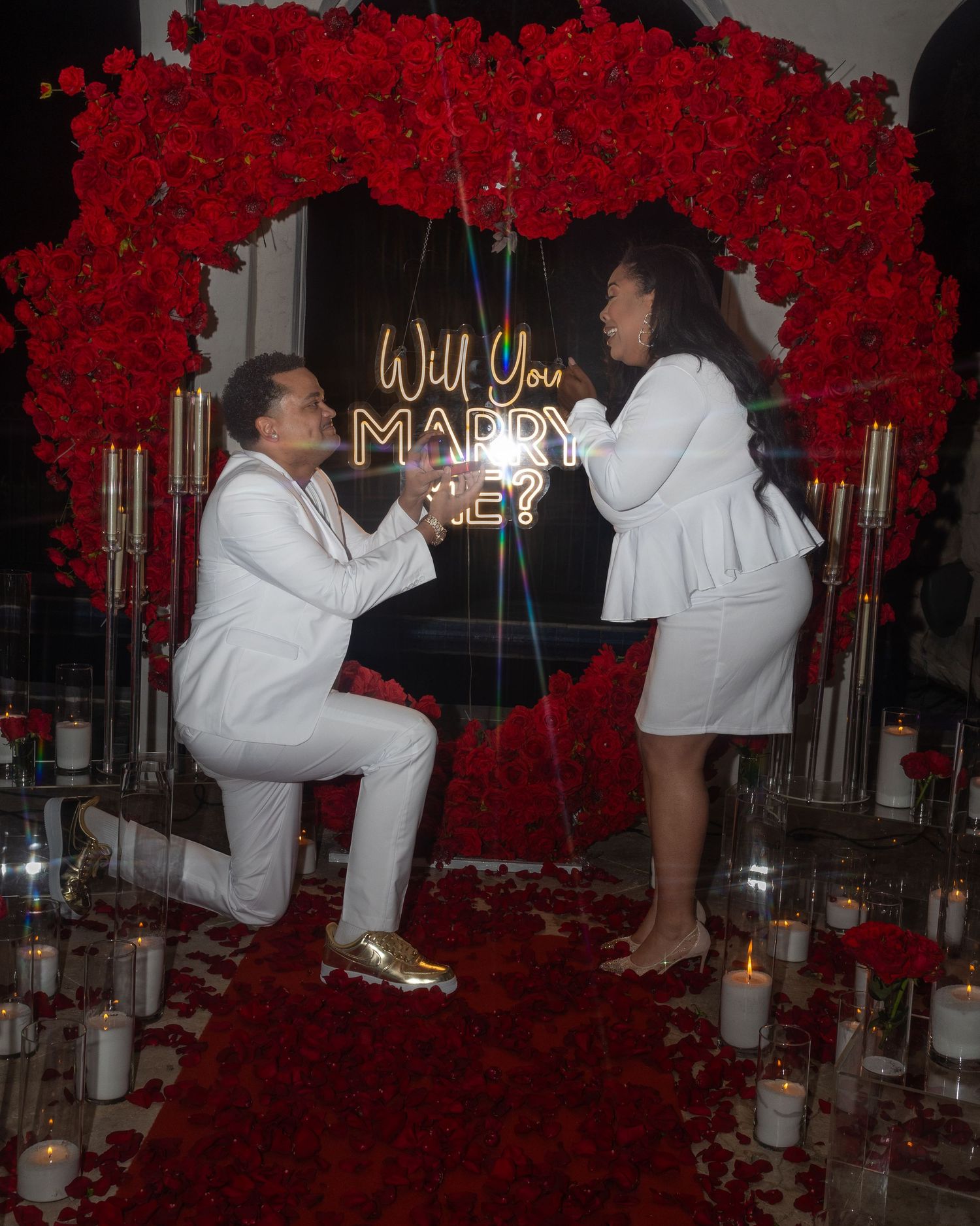 Romantic proposal setup with red rose decor and white candles arranged in a dimly lit room.
