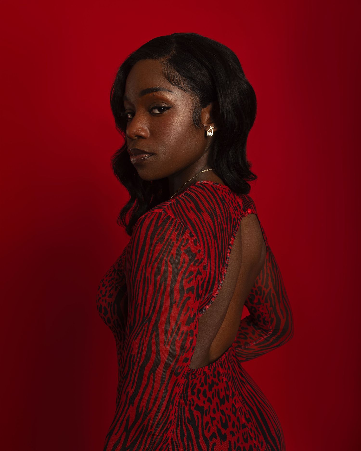 Fashion portrait against deep red background featuring a black and red striped dress.