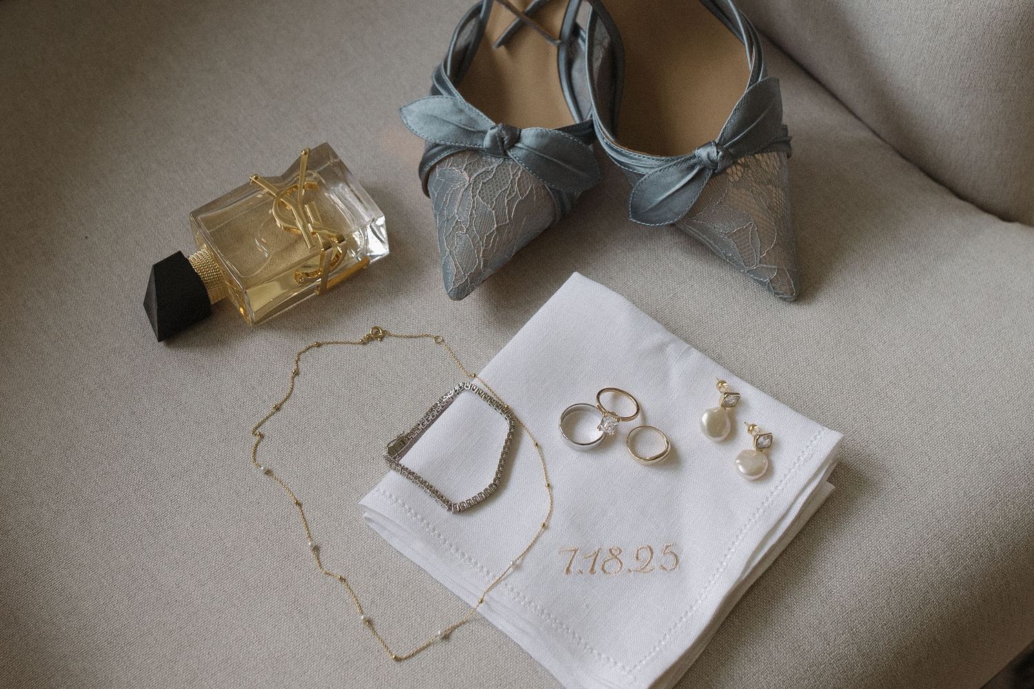Wedding accessories including rings, shoes, and stationery arranged on neutral fabric.