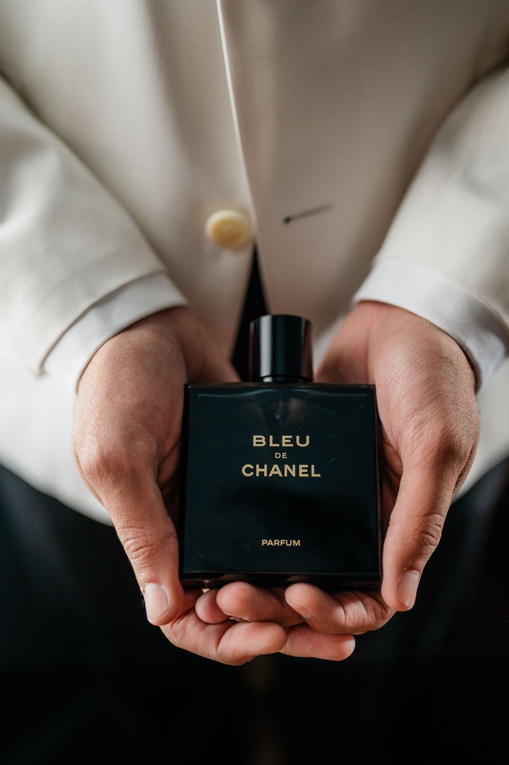 Hands holding a black Bleu de Chanel perfume bottle against a white background.