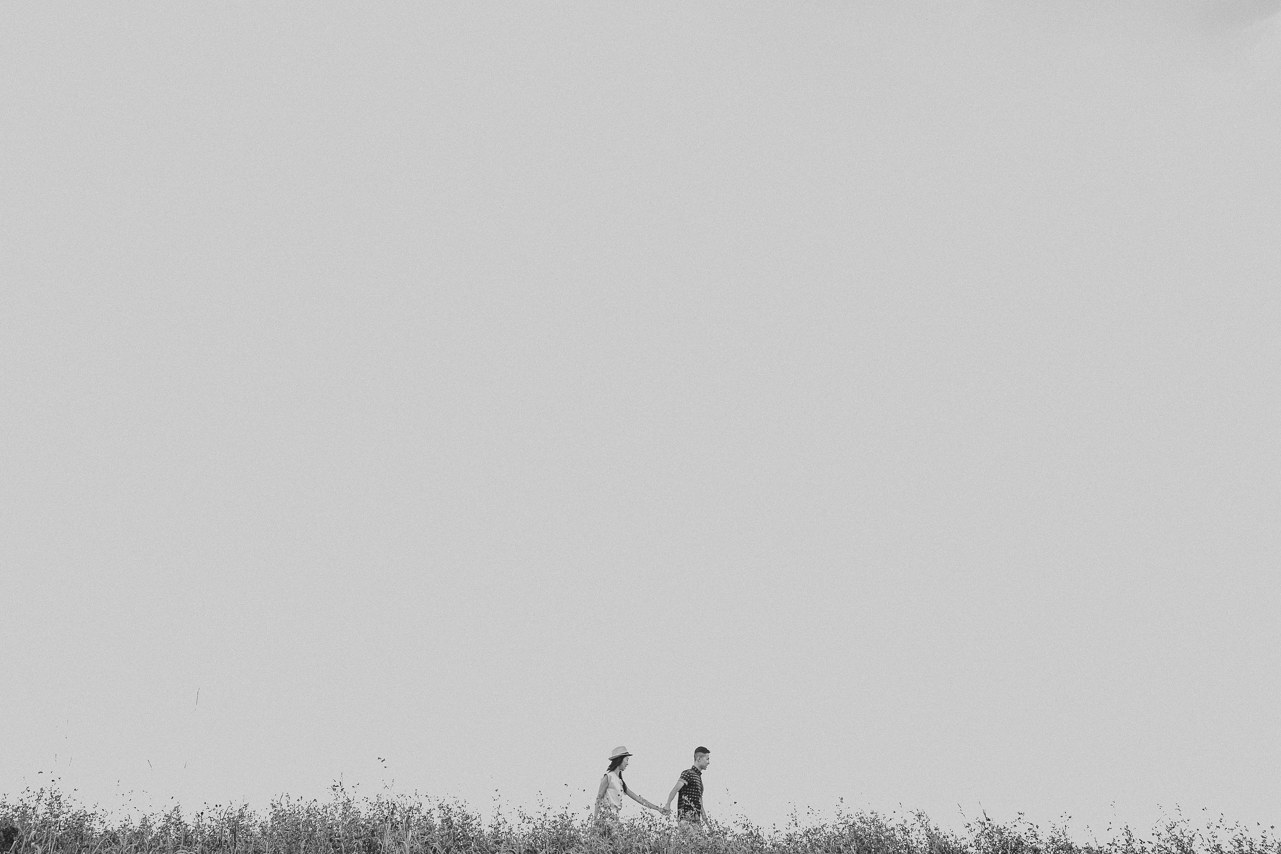 Two people stand on a grassy hilltop silhouetted against a bright sky at sunset.
