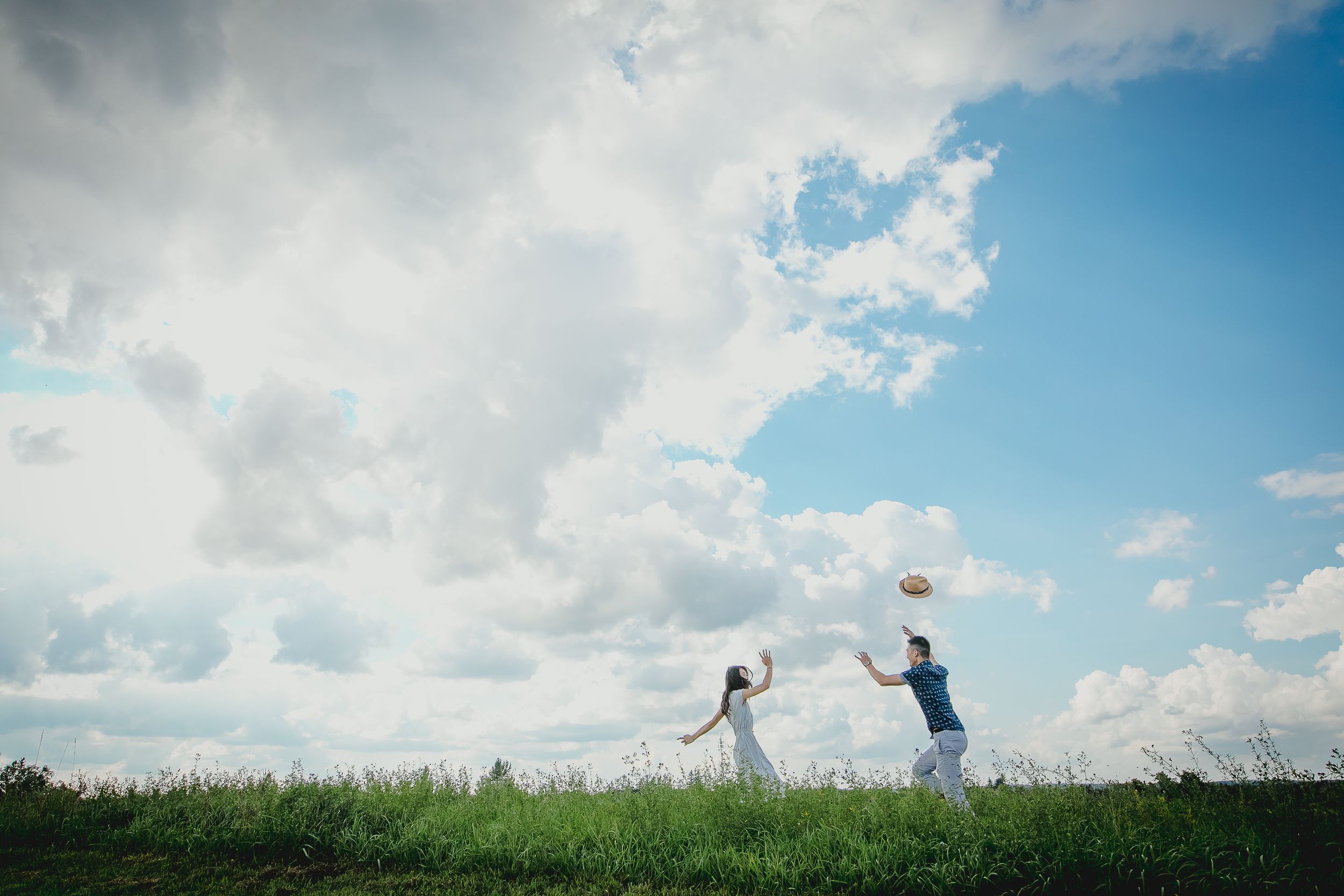 Couple embraces against dramatic cloudy sky backdrop during outdoor photoshoot.