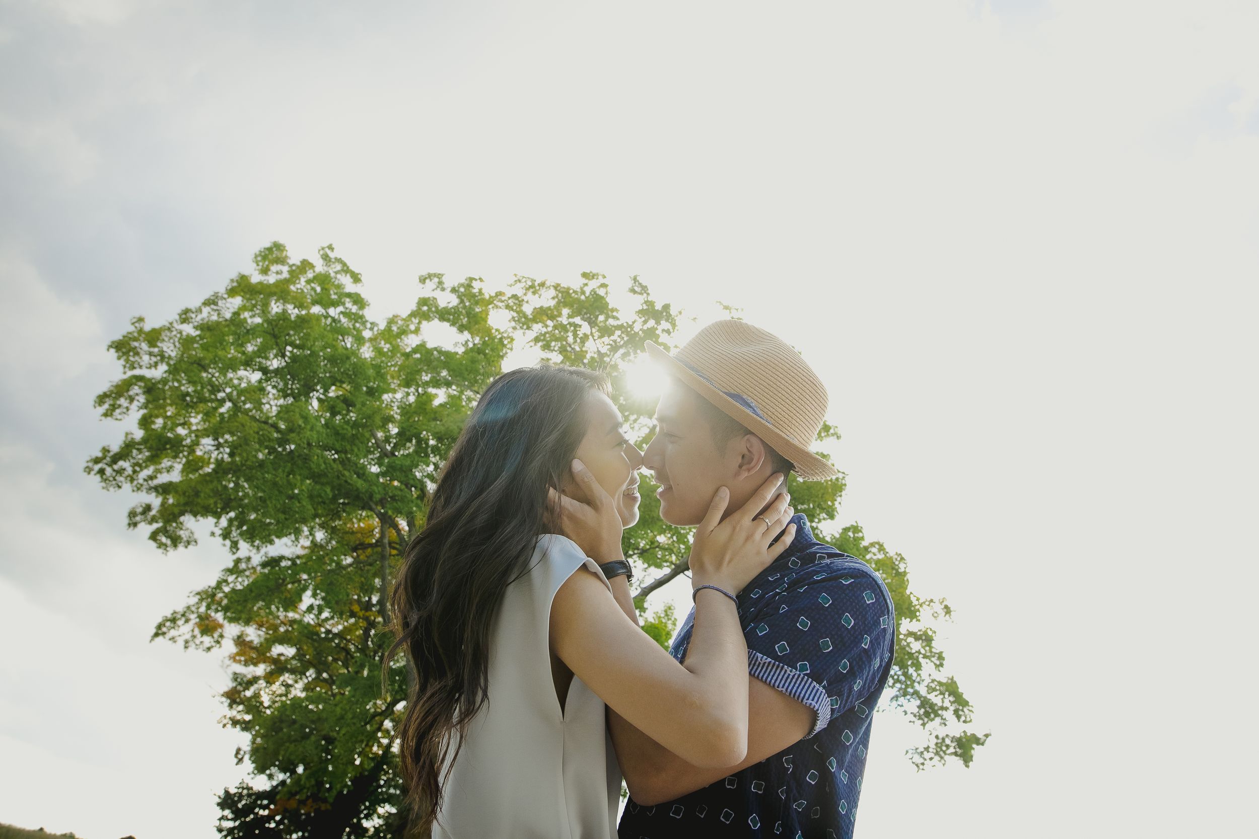 A couple shares a romantic moment in a sunlit outdoor setting surrounded by greenery.