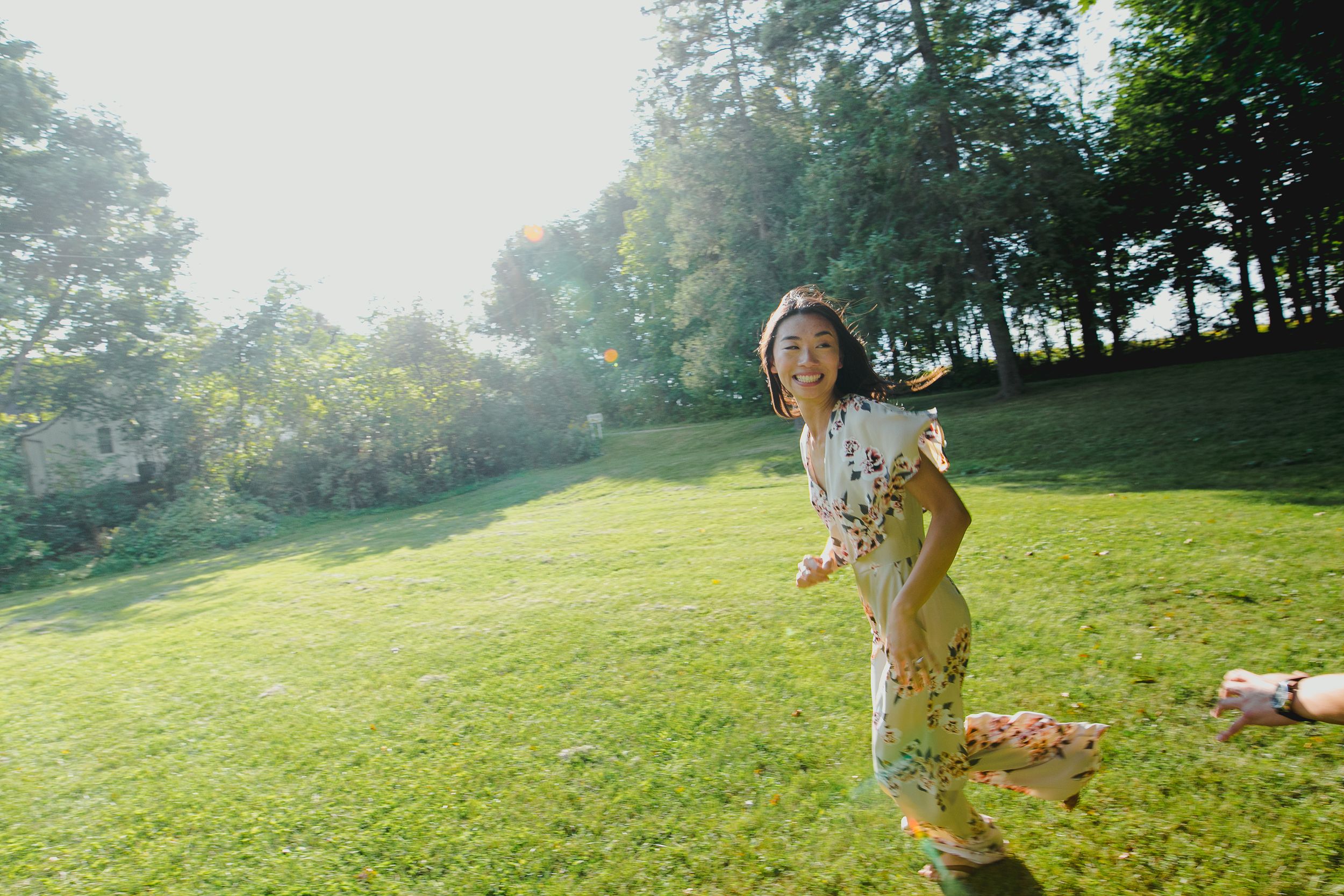 A group enjoys outdoor activities on a sunlit grassy hillside surrounded by trees.