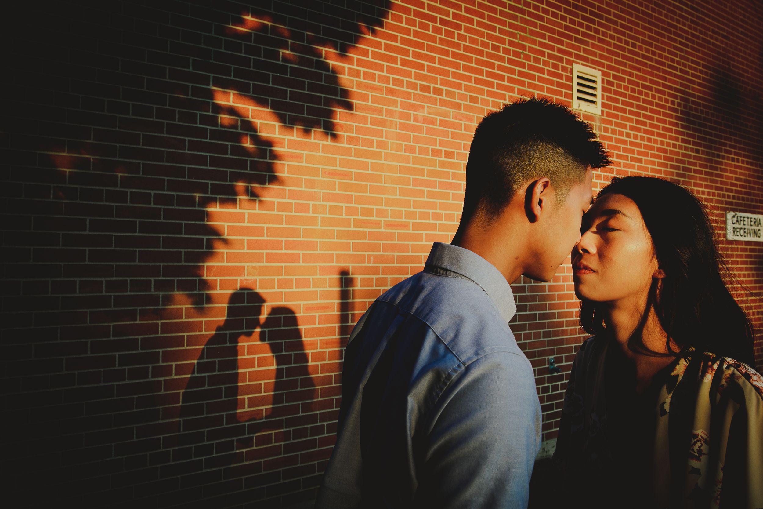 Romantic silhouettes against a brick wall illuminated by warm sunset lighting.