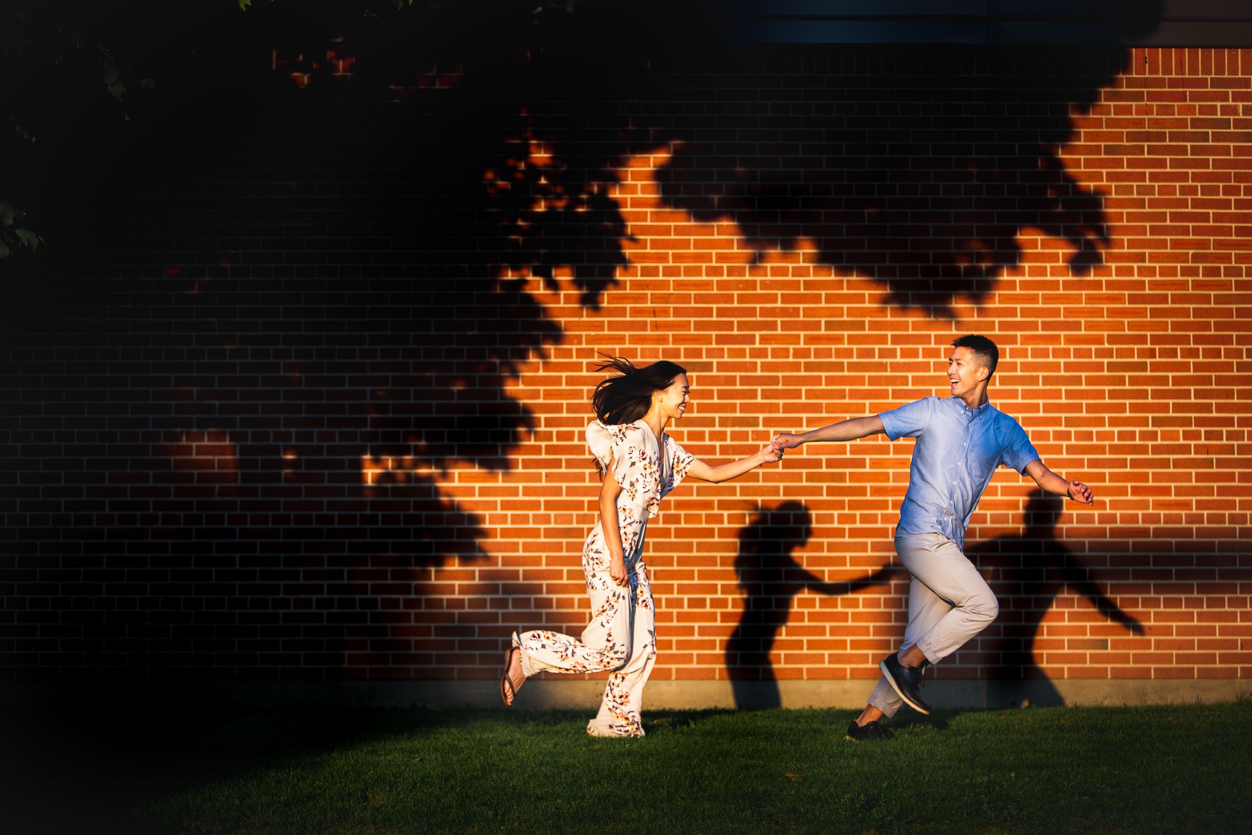 Silhouettes of people playfully posing against an orange-lit brick wall at sunset.