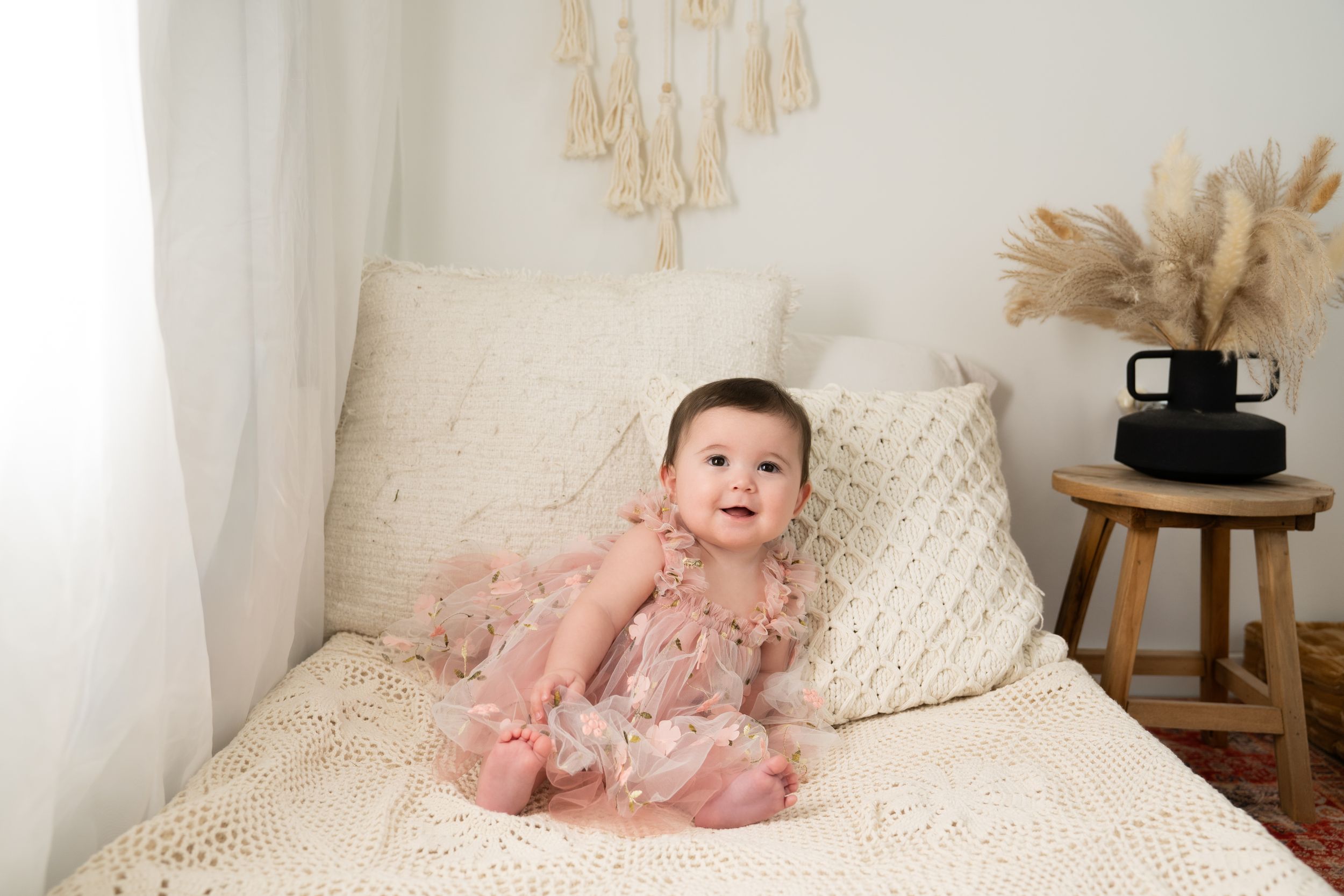 An infant in a delicate pink outfit poses on a white knit blanket.