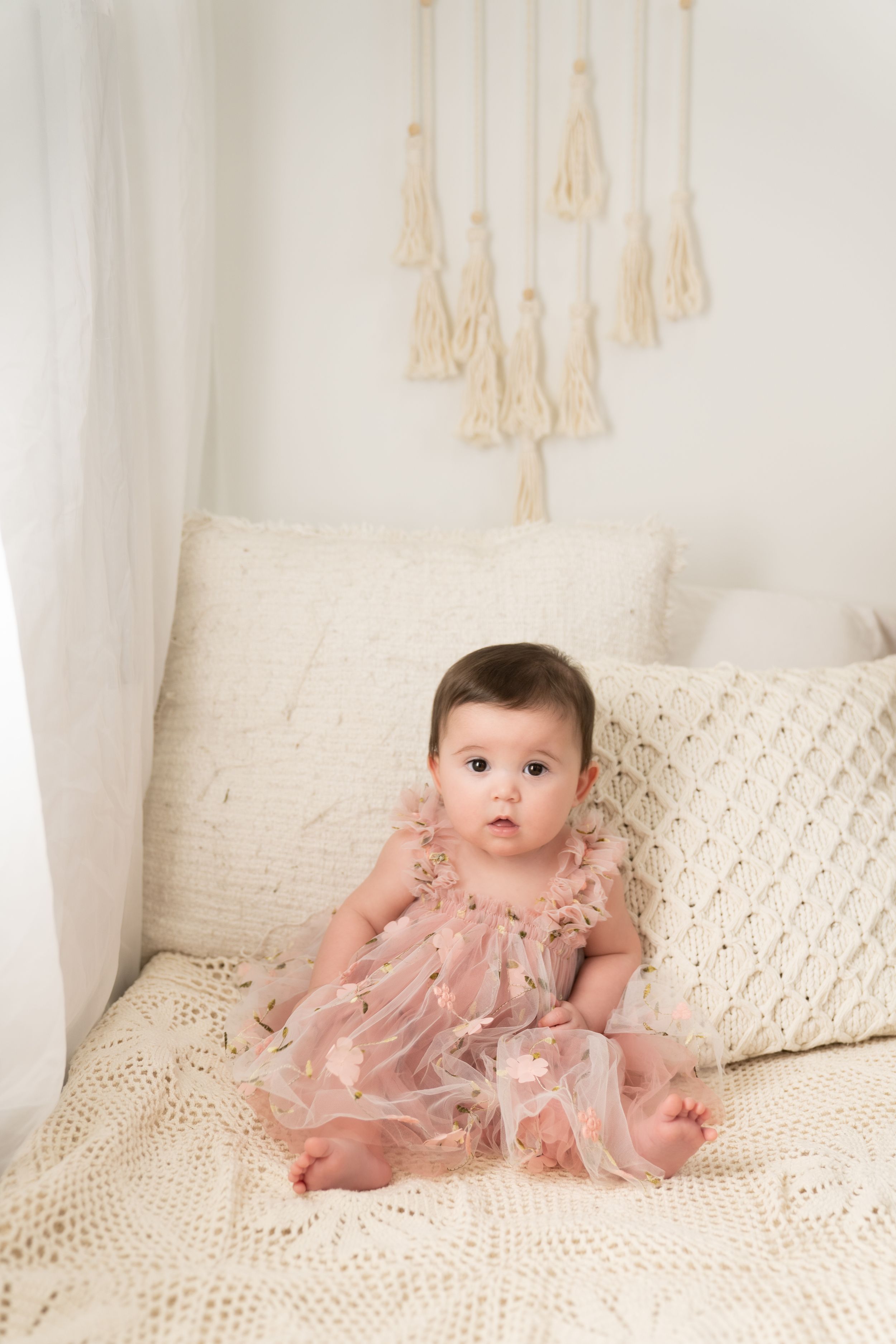 A baby wearing a pink tulle dress sits on a textured white bedspread.