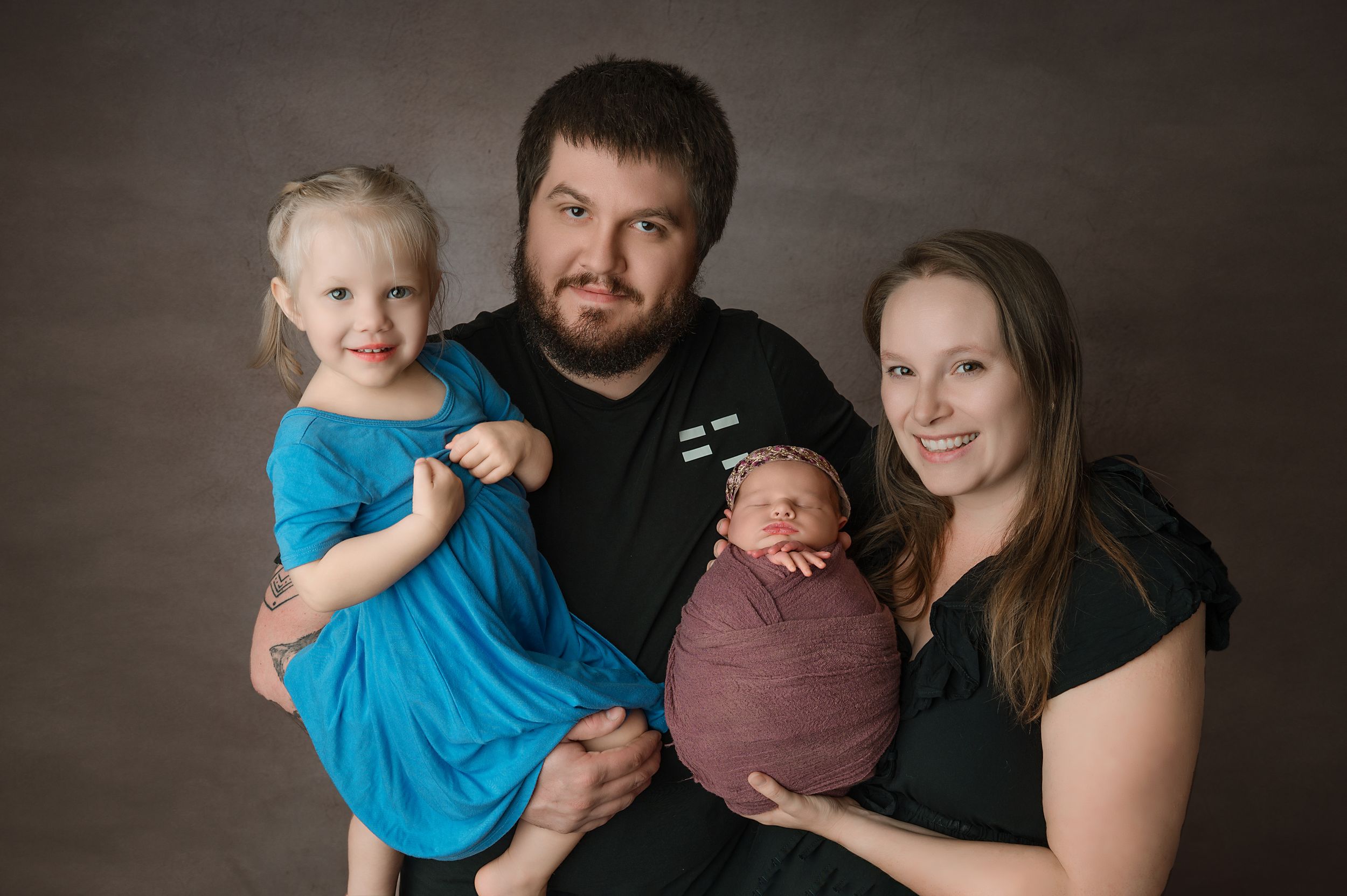 Two adults pose with a small child against a dark studio backdrop in complementary brown and blue clothing.